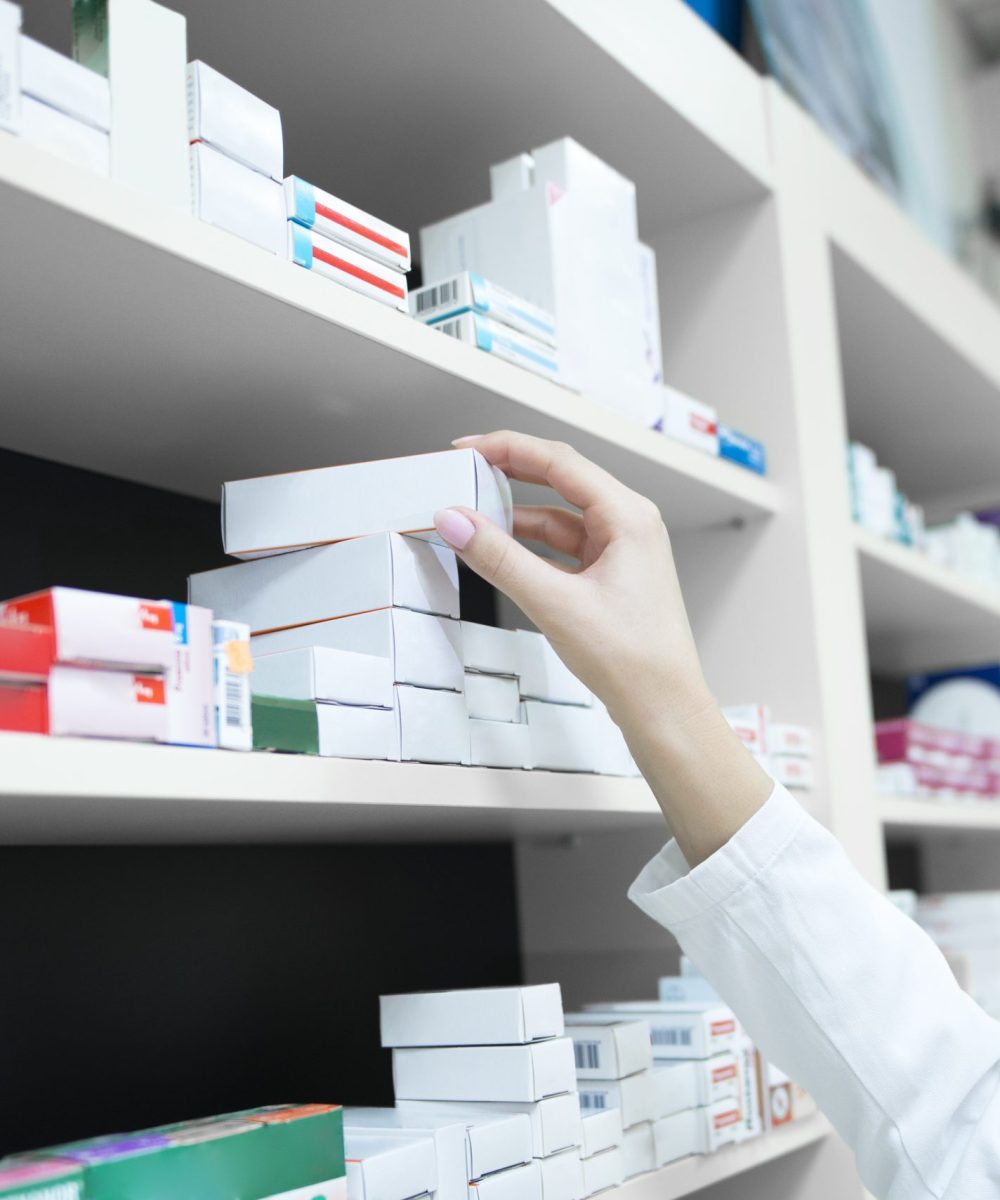 Closeup view of pharmacist hand taking medicine box from the shelf in drug store.
