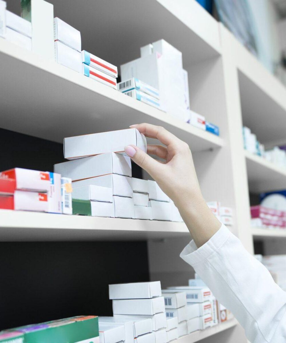 Closeup view of pharmacist hand taking medicine box from the shelf in drug store.