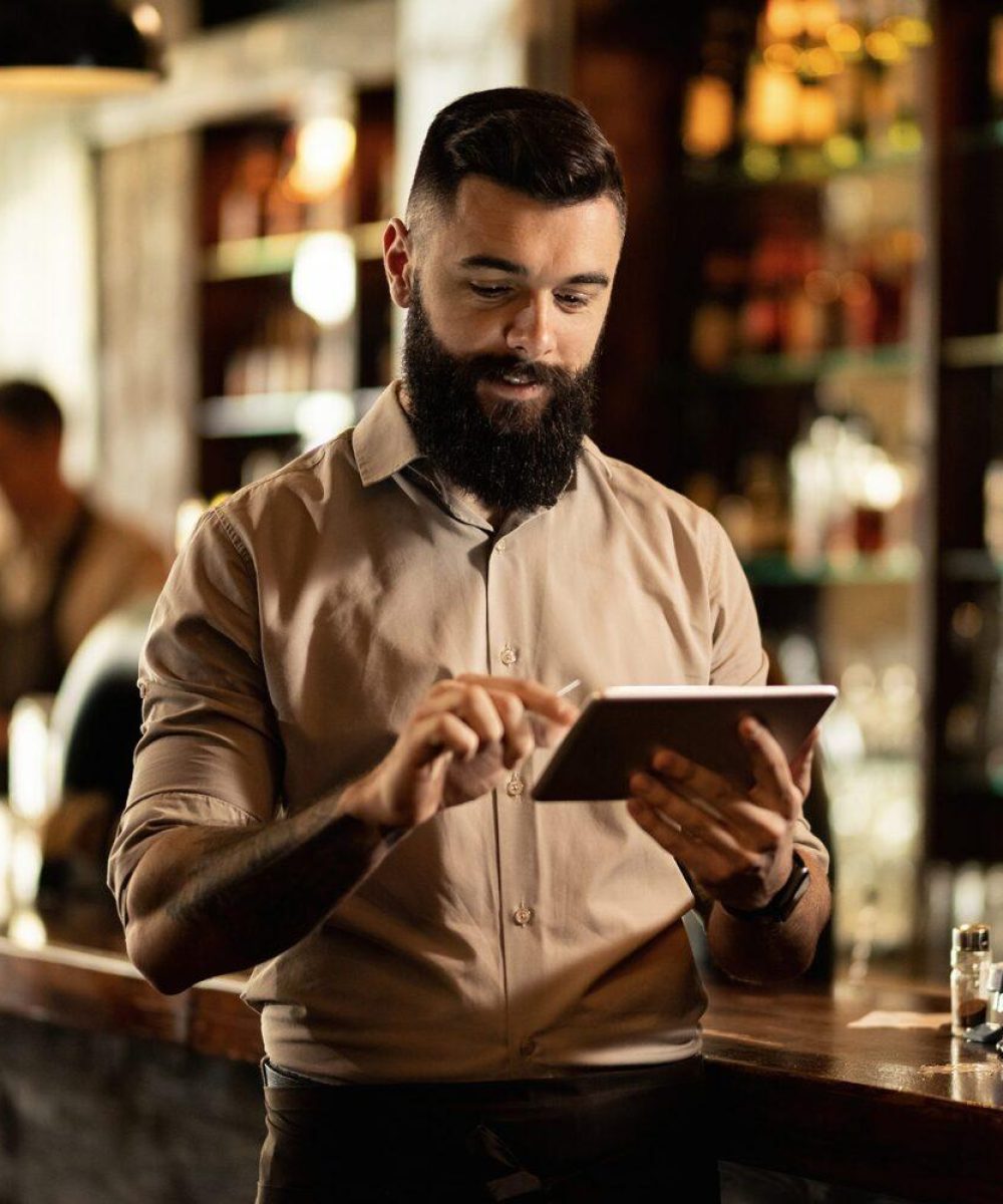 Smiling barista using digital tablet while working in a bar.